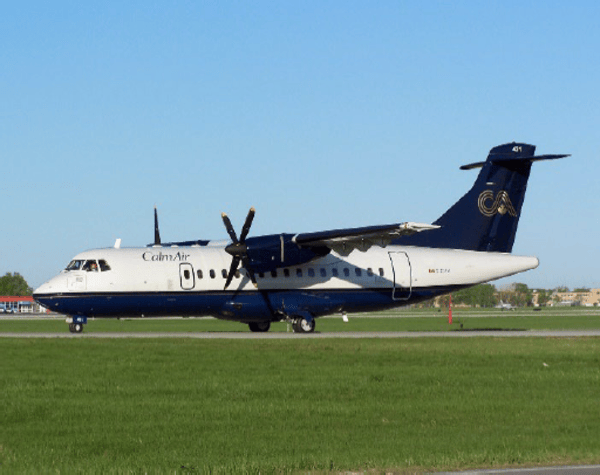 Een turbopropvliegtuig van Calm Air met een blauw-witte kleurstelling, uitgerust met een Garmin GTX-3000 ADS-B-transponder, staat geparkeerd op de start- en landingsbaan, met op de voorgrond groen gras en op de achtergrond een helderblauwe lucht.
