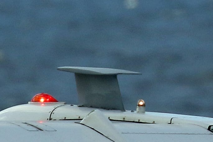 Een close-up van de UHF-satellietcommunicatieantenne van een vliegtuig bovenop de romp, met brandende rode en oranje navigatielichten en een wazige lucht of zee op de achtergrond, illustreert een recente upgrade van de missiesystemen.