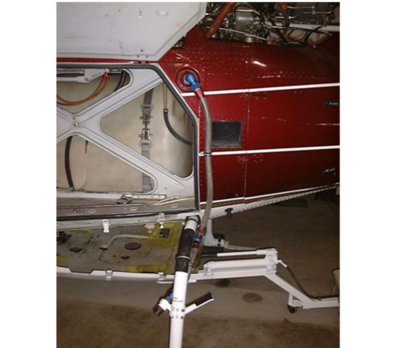 A close-up view of a helicopter’s fuselage with an access panel open, showing internal components. A fuel hose is connected to the Hot Refuel System for rapid refueling, with equipment positioned on the floor nearby.