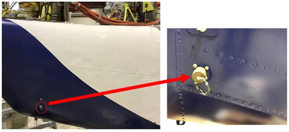 A white and blue aircraft fuselage with a red arrow pointing to a close-up of a round, beige access panel secured by screws—this panel houses the 24 VDC auxiliary power connector.