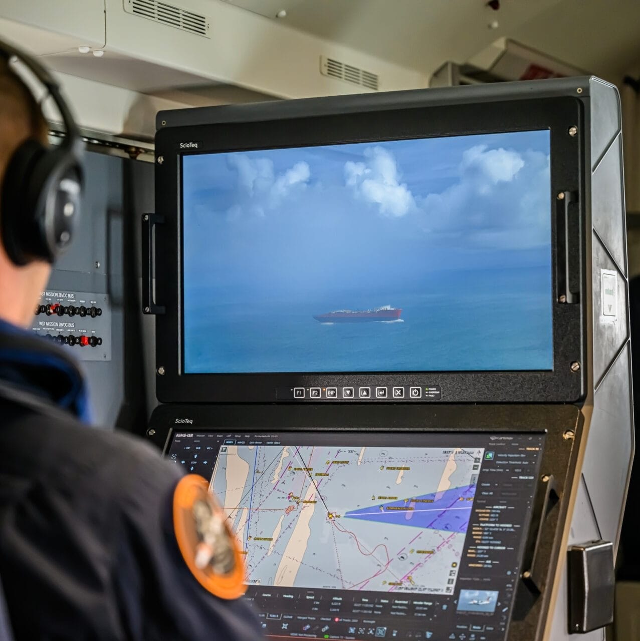 Una persona con auriculares supervisa un barco en una pantalla grande y consulta mapas de navegación en otra, probablemente en una sala de control, mientras supervisa las operaciones marítimas de la Guardia Costera de los Países Bajos.