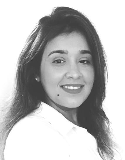 Retrato en blanco y negro de una mujer de pelo largo, sonriente, con una blusa de color claro, mirando ligeramente hacia la derecha y con un lunar visible en la mejilla; su expresión serena refleja la precisión de la vigilancia medioambiental.