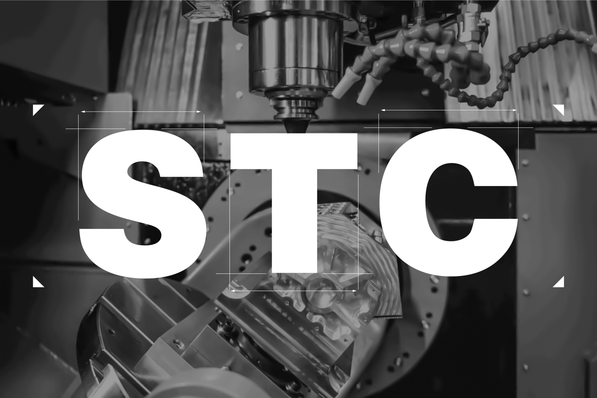 Tehase keskkonnas katavad suured valged tähed „STC“ tööstuslikku CNC-masinat, rõhutades seadme paigaldamist halltoonides kujutatud mehaaniliste komponentide ja metallkonstruktsioonide keskel.