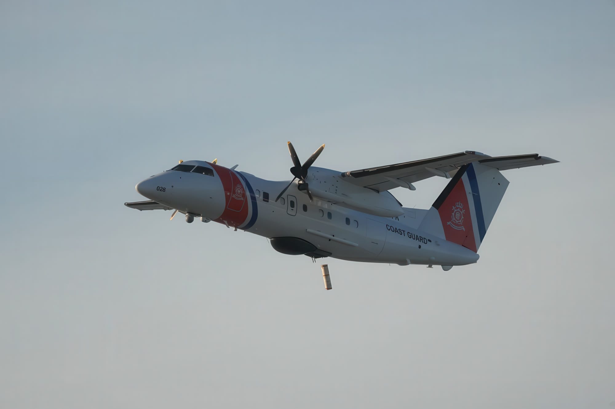 A U.S. Coast Guard Dash-8 Fleet aircraft with red and blue markings flies in a clear sky, viewed from the side with its landing gear retracted and propellers spinning during a search and rescue mission.