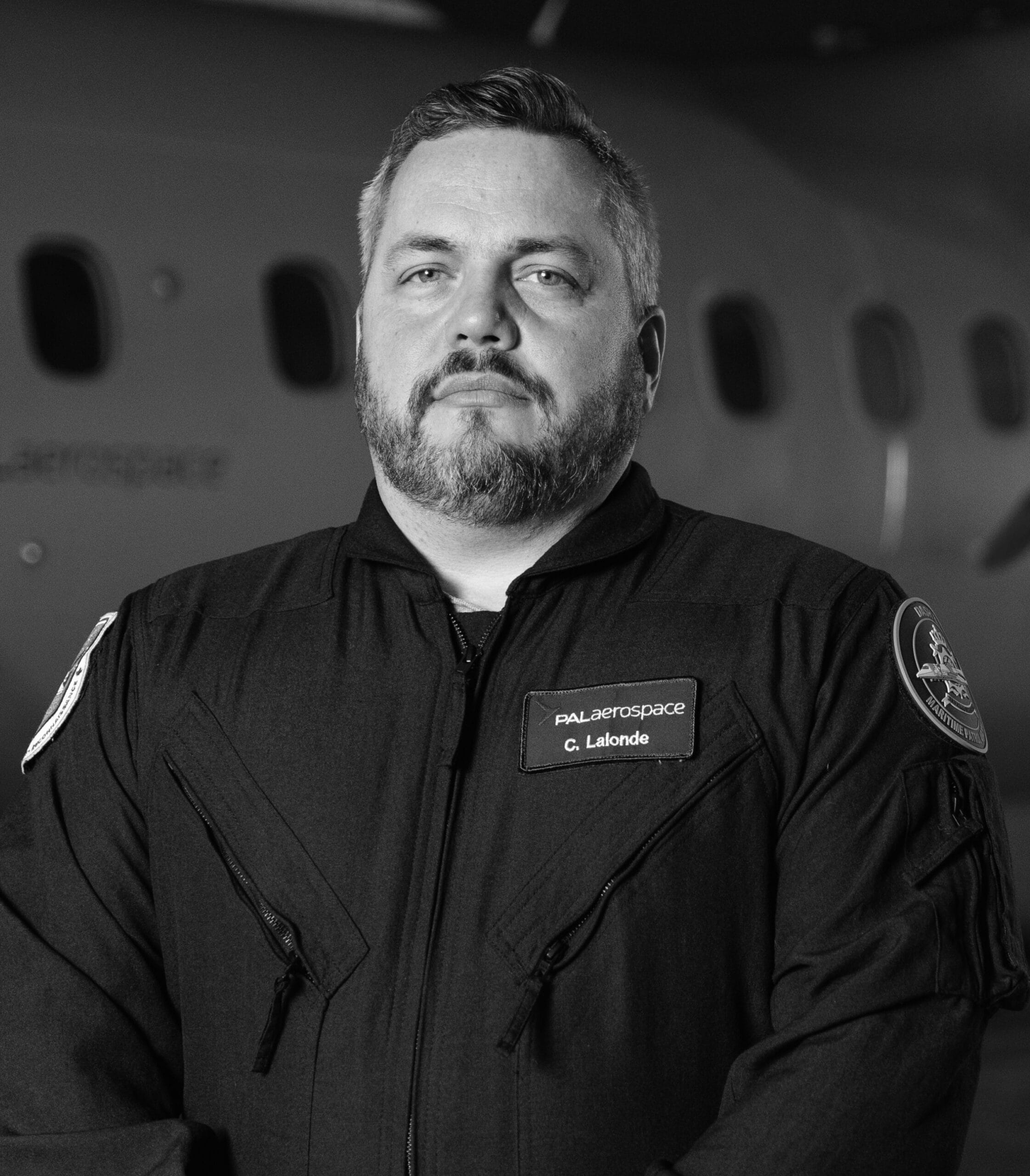 Op een zwart-witfoto staat een man met een baard en kort haar, gekleed in een pilotenpak met PAL Aerospace-emblemen en een naamplaatje met de naam G. Lalonde, voor een vliegtuig.